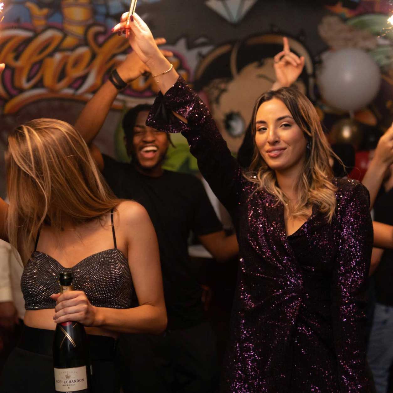 two girls dancing and holding a bottle of champagne