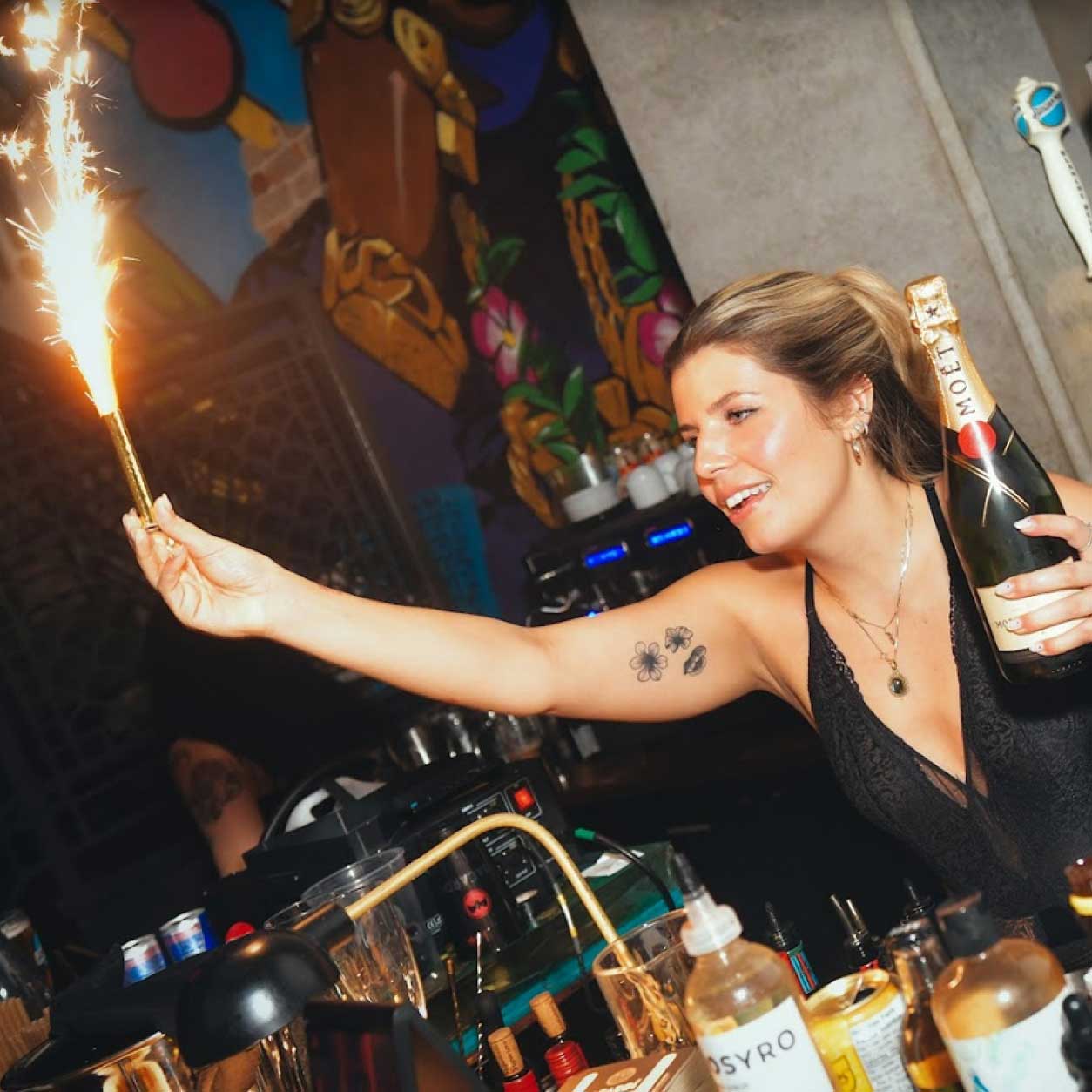 young woman holding a light sparks and a bottle of champagne